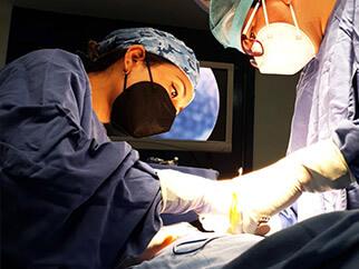 Dra. Irasema Salgado Falcón con bata azul, gorro y cubrebocas negro, operando junto a colega