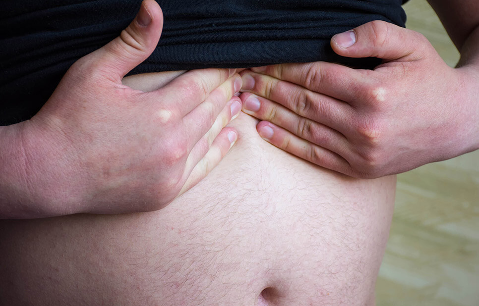 Hombre con playera negra, tocando su estómago a la altura del diafragma para detectar una hernia hiatal, padecimiento tratado por la Dra. Irasema Salgado Falcón